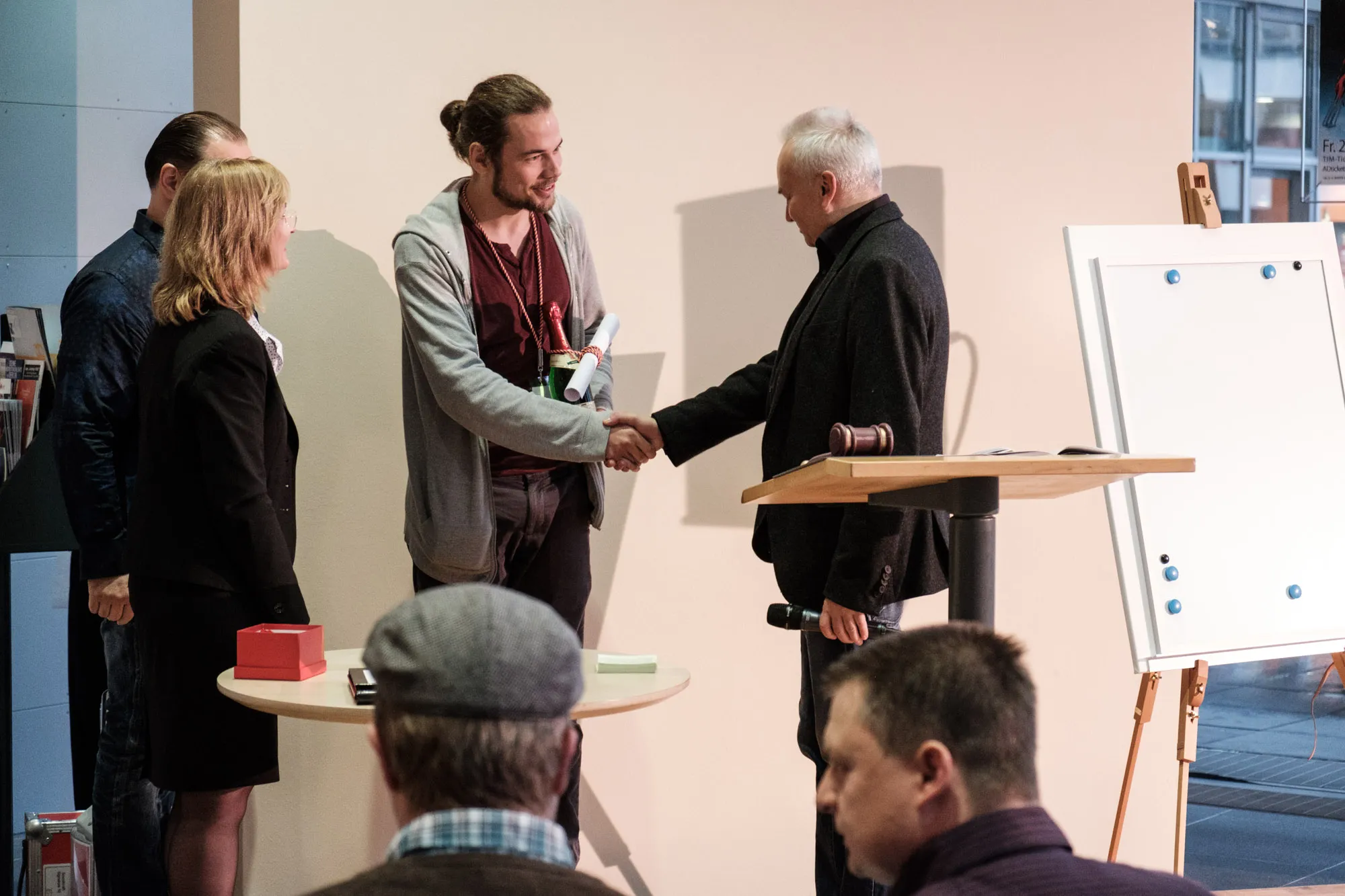 Ein älterer Herr übergibt einen Messepreis an einen jungen Mann.